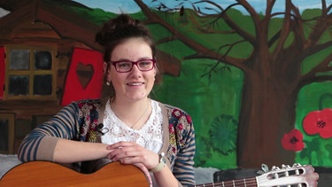 Bernadette stützt sich auf ihre Gitarre und lacht | Bild: Bayerischer Rundfunk