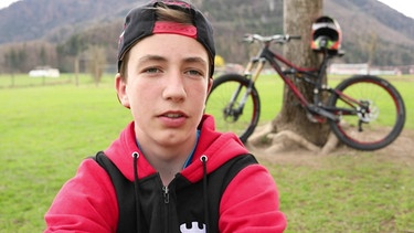 Wolfi erzählt, im Hintergrund lehnt sein Rad an einem Baum | Bild: Bayerischer Rundfunk