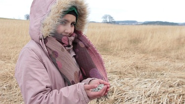 Hadaya steht vor einem Feld und hält Steine in ihren Händen. | Bild: Bayerischer Rundfunk