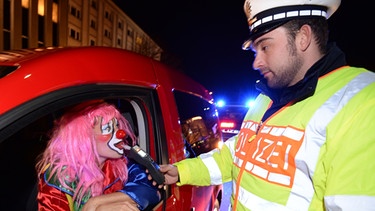 Ein Polizist kontrolliert eine als Clown verkleidete Frau in ihrem Auto auf Alkohol. | Bild: picture-alliance/dpa