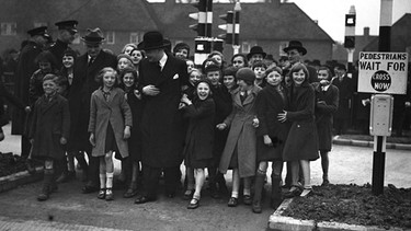 Ein Bild aus dem Jahr 1936 zeigt den englischen Verkehrsminister, Leslie Hore-Belisha, wie er mit einer großen Schar Kinder die "neue" Ampelanlage ausprobiert. | Bild: picture alliance / AP Images | RID