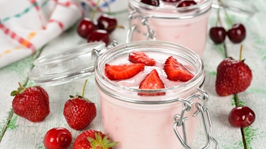 Gläser mit Joghurt und frischen Erdbeeren bzw. Kirschen stehen auf einem Tisch. | Bild: colourbox.com