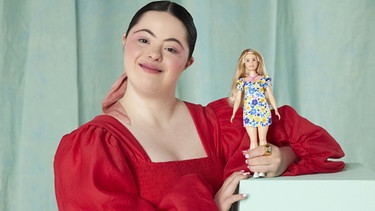 Das Model Ellie Goldstein im April 2023 mit der ersten Barbie-Puppe mit Down-Syndrom. Die Puppe mit langen Haaren, einer pinkfarbenen Kette und einem bunten Blumenkleid solle "mehr Kindern ermöglichen, sich selbst in Barbie widergespiegelt zu sehen, und Barbie ermöglichen, die Welt um sie herum widerzuspiegeln", hieß es von Mattel. | Bild: dpa-Bildfunk/Catherine Harbour/Mattel