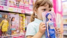 Ein kleines Mädchen hält in einem Spielzeugladen eine verpackte Barbie-Puppe (als Meerjungfrau) in den Händen. | Bild: colourbox.com