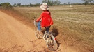 Das Mädchen Tona fährt mit ihrem Fahrrad zwischen riesigen abgeernteten Reisfeldern  | Bild: BR | Waldenburg