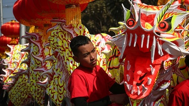 Ein Künstler aus Kathmandu in Nepal bereitet sich neben einer Drachenskulptur auf die Aufführung eines Drachentanzes vor. Anlass ist die Parade zum chinesischen Neujahrsfest in das Jahr des Drachen. | Bild: Sunil Sharma/ZUMA Press Wire/dpa