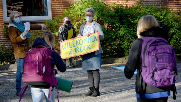 Mit einem Schild "Willkommen zurück" begrüßt eine Lehrerin die Viertklässler in der Grundschule.  | Bild: dpa-Bildfunk/Carsten Rehder