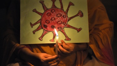 Ein Kind hält eine brennende Kerze vor einer Zeichnung des Coronavirus. Indiens Premierminister Modi hat die Bürger seines Landes gebeten, Lichter gegen die Dunkelheit in der Coronavirus-Pandemie anzuzünden.  | Bild: dpa Picture alliance