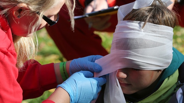 Ein Mädchen legt einem Jungen einen Kopfverband an. | Bild: picture-alliance/dpa