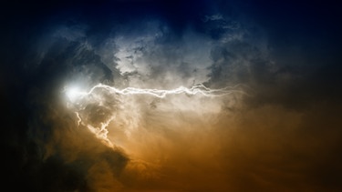 Ein Blitz entlädt sich in einem blau-gelben Wolkenhimmel. | Bild: stock.adobe.com/IgorZh