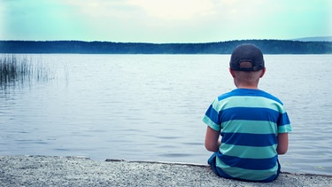 Junge sitzt allein am Uferrand und blickt auf den See | Bild: colourbox.com