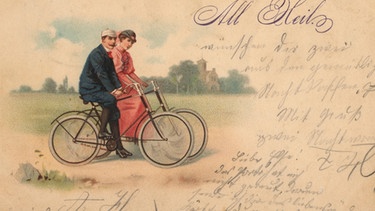 Historische Postkarte mit einem Pärchen auf Fahrrädern. | Bild: picture-alliance/dpa