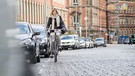 Fahrradfahrerin fährt auf der Straße an parkenden Autos vorbei. | Bild: picture-alliance/dpa
