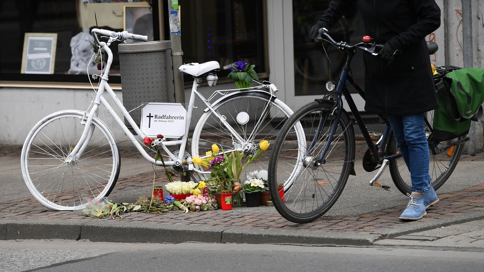 Eine Radfahrerin steht in der Innenstadt von Darmstadt (Hessen) an einer belebten Straße neben einem weißen Geisterrad, das an eine verunglückte Radfahrerin erinnern soll. | Bild: dpa-Bildfunk/Arne Dedert