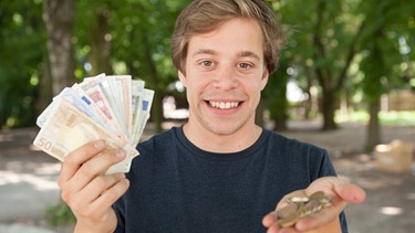 Checker Tobi hält in der einen Hand Geldscheind und in der andere Münzen. | Bild: megaherz