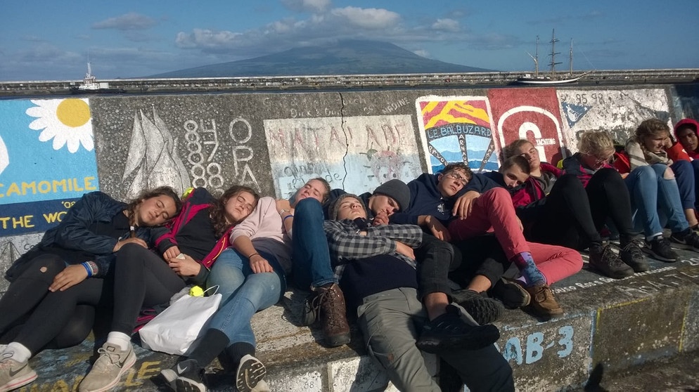 Die Mitglieder des Ocean College dösen in der Sonne an der Hafenmauer von Horta. | Bild: Ocean College