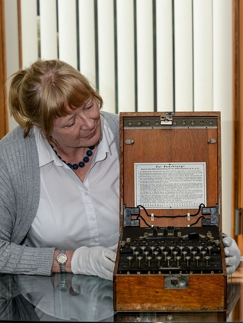 Eine Frau präsentiert eine Enigma-Schreibmaschine. Im Zweiten Weltkrieg wurden damit geheime Botschaften verschlüsselt. | Bild: picture-alliance/dpa