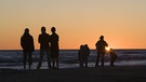 Die Schattenrisse einer Familie vor einem Sonnenuntergang am Meer. | Bild: picture-alliance/dpa