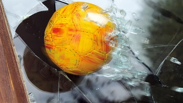 Ein Fußball fliegt durch eine zersplitternde Fensterscheibe. | Bild: MEV/Eckart Seidl