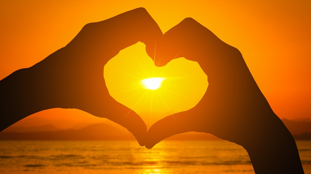 Zwei Hände formen ein Herz vor einem Sonnenuntergang am Meer. | Bild: colourbox.com