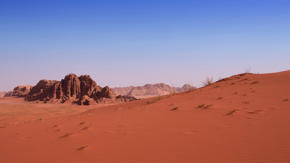 Eine rote Sanddüne mit einem felsigen Hintergrund in der Wüste Wadi Rum. Dieses Foto stammt von der Erde! | Bild: colourbox.com
