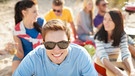 Eine Gruppe von Erwachsenen am Strand. Vorne ein lächelnder Mann mit Sonnenbrille. | Bild: colourbox.com