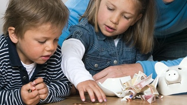 Kinder und Vater zählen Geld aus zerschlagenem Sparschwein.  | Bild: MEV/Sven Lüders