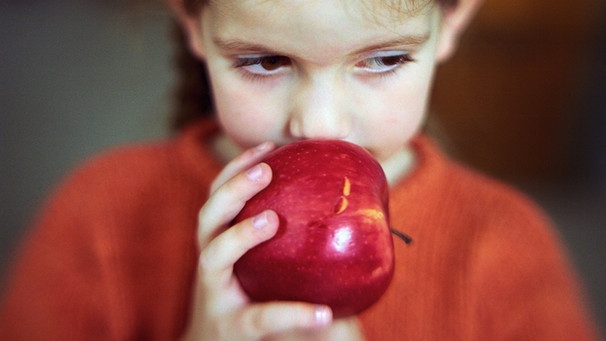 Ein Mädchen hält einen Apfel an den Mund. | Bild: colourbox.com