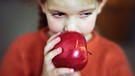 Ein Mädchen hält einen Apfel an den Mund. | Bild: colourbox.com