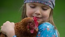 Ein Mädchen hält ein Huhn im Arm. | Bild: picture-alliance/ZB