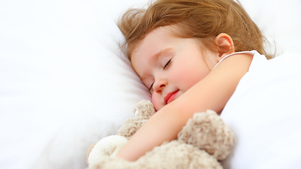 Ein Mädchen schläft mit seinem Kuscheltier im Bett. | Bild: colourbox.com