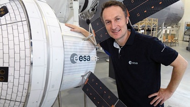 Der Astronaut Matthias Maurer steht im Europäischen Astronautenzentrum (EAC) auf dem Gelände der ESA neben einem Modell der Raumkapsel Orion.  | Bild: picture alliance/Felix Hörhager/dpa