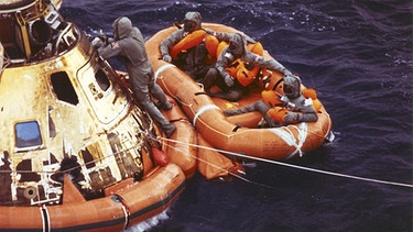 Archiv: Leutnant Clancy Hatleberg schließt die Luke der Apollo 11, während die Astronauten Neil Armstrong, Michael Collins und Buzz Aldrin auf ihrer Rettungsinsel sitzen. Sie warten auf die Abholung durch einen Hubschrauber, nachdem sie nach ihrer erfolgreichen Mondmission im Pazifik gelandet sind. Aufgenomen am 23.07.1969. | Bild: dpa-Bildfunk | Milt Putnam