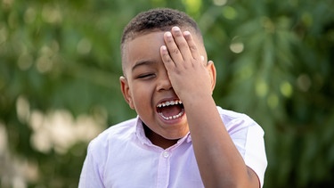 Ein Junge hält sich lachend mit der Hand ein Auge zu. | Bild: colourbox.com
