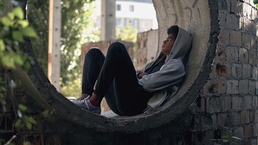 Ein Junge mit Kaputzenpulli sitzt in einer Mauernische. | Bild: colourbox.com