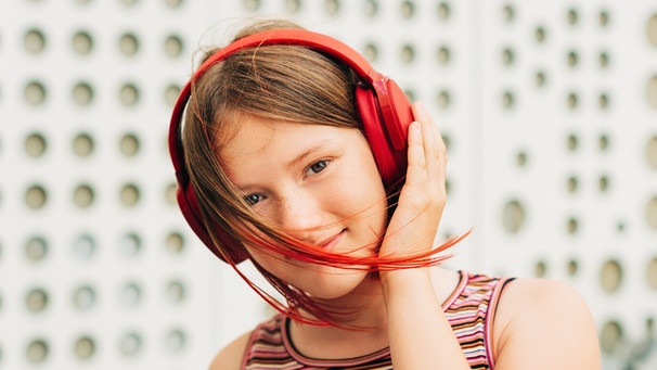 Ein Mädchen mit Kopfhörern und rot gefärbten Haaren blickt freundlich in die Kamera. | Bild: colourbox.com