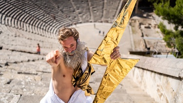 Der Alte-Griechen-Check | Tobi ist als der Wettergott Zeus verkleidet und steht im antiken Theater in Epidauros. | Bild: BR | megaherz gmbh | Hans-Florian Hopfner