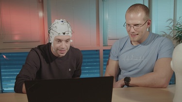Der Gehirn-Check | Dr. Alex Kreilinger (rechts) zeigt Tobi, wie er mit seinen Gedanken am Computer Wörter schreiben kann. Tobi hat ein Brain-Computer-Interface auf. | Bild: BR | megaherz gmbh