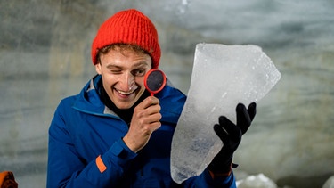 Erforsche den Gletscher | Julian erforscht mit einer Lupe ein Stück Gletschereis.  | Bild: BR | megaherz gmbh | Franziska Gruber