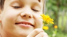 Ein Junge riecht mit geschlossenen Augen an einer Blume. | Bild: colourbox.com