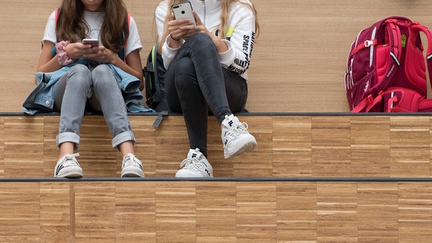 Schülerinnen sitzen im Foyer eines Gymnasium auf einer Freitreppe und halten jeweils ein Smartphone in der Hand. | Bild: dpa-Bildfunk/Sebastian Kahnert