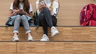 Schülerinnen sitzen im Foyer eines Gymnasium auf einer Freitreppe und halten jeweils ein Smartphone in der Hand. | Bild: dpa-Bildfunk/Sebastian Kahnert