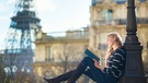 Eine junge Frau liest angelehnt an eine Straßenlaterne. Im Hintergrund ist der Eifelturm zu sehen. | Bild: colourbox.com