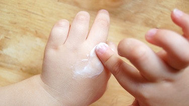 Ein Kind cremt sich die Hände mit Sonnencreme ein. | Bild: stock.adobe.com/thingamajiggs