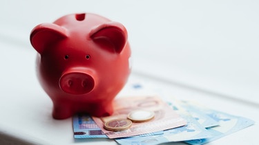 Ein rotes Sparschwein mit Geld. | Bild: BR/Julia Müller