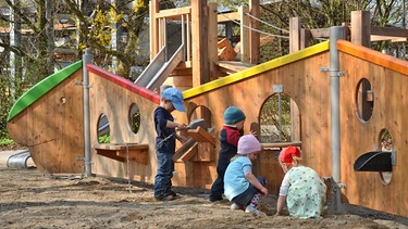 Kleinkinder spielen vor einer Holzinstallation im Sand auf dem Spielplatz in Frasdorf. | Bild: Richter Spielgeräte