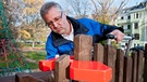 Ein Prüfer untersucht die Abstände der Holzlatten eines Zaunes an einem Spielplatz. | Bild: TÜV Rheinland