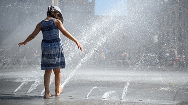 Ein Mädchen spielt am 1.8.2017 am Springbrunnen am Stachus in München (Bayern) mit den Wasserfontänen. | Bild: picture alliance / Matthias Balk/dpa