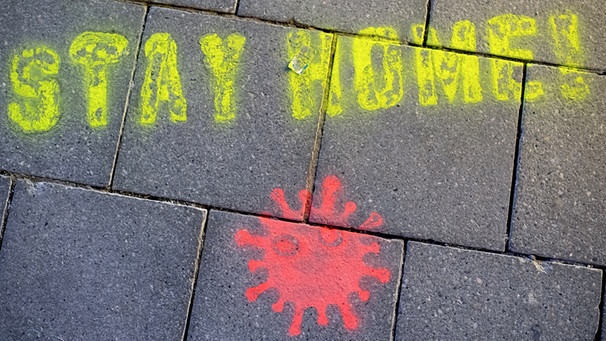 Ein Graffiti mit "Stay Home" (bleib zu Hause) und einem Virus auf einer Straße in München. | Bild: picture-alliance/dpa