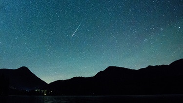 Eine Sternschnuppe leuchtet neben der Milchstraße am Himmel über dem Walchensee. Jedes Jahr im August sind im Sternschnuppenstrom der Perseiden zahlreiche Sternschnuppen zu sehen. Aufgenommen am 12.08.2018 in Einsiedl in Bayern. | Bild: picture-alliance/dpa
